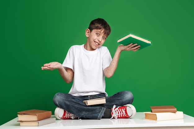 Cheerful young boy with freckles choosing between book and empty copyspace while looking at the front over green wall