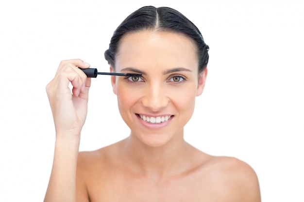 Cheerful young brunette applying mascara