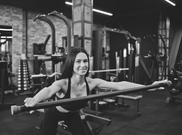 Cheerful young brunette in sportwear doing gymnastic exercise with  body bar in her hand in gym