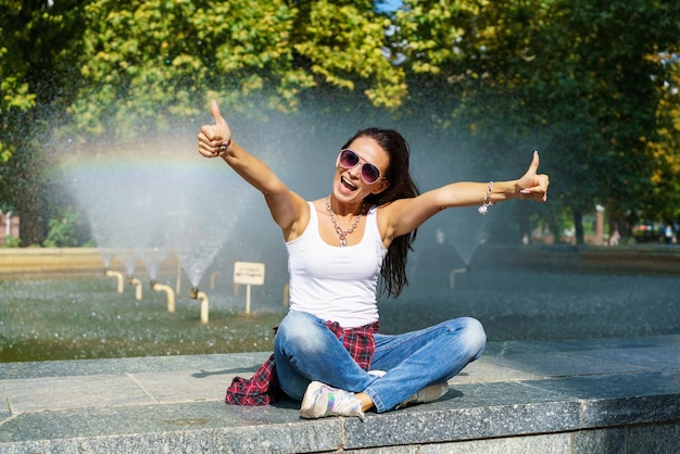 Cheerful young brunette woman against background fountain happy shows gesture