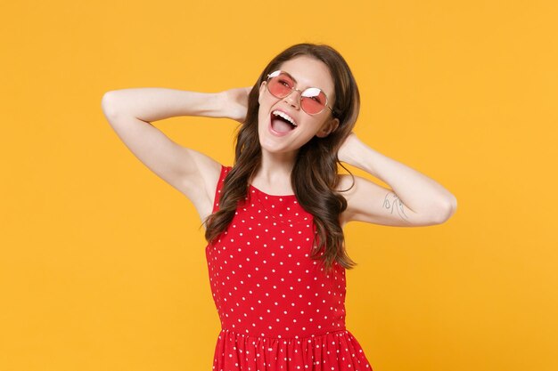 Cheerful young brunette woman girl in red summer dress eyeglasses posing isolated on yellow backgrou