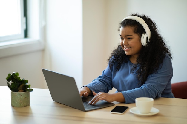 Cheerful young brunette woman using wireless headphones laptop at home