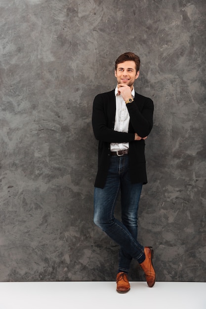 Cheerful young businessman standing over grey wall