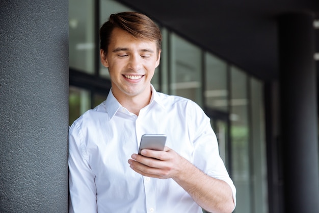 Cheerful young businessman talking on mobile phone near business center