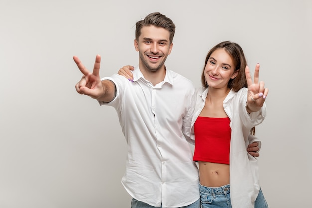 Cheerful young caucasian couple standing on white background showing peace sign