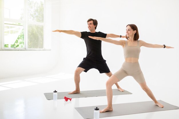 Cheerful young caucasian lady and guy in sportswear enjoy workout together practice yoga with water