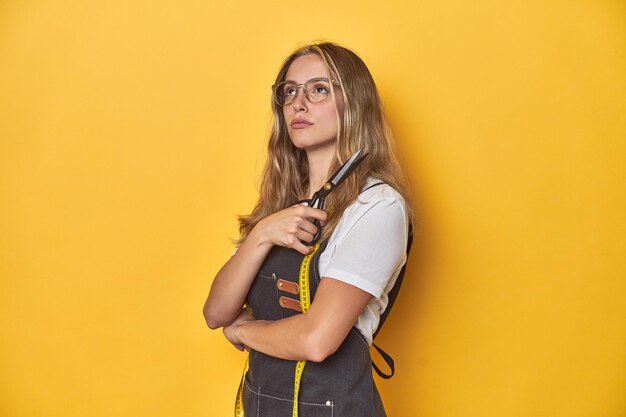 Cheerful young Caucasian stylist holding scissors on a vibrant yellow studio backdrop