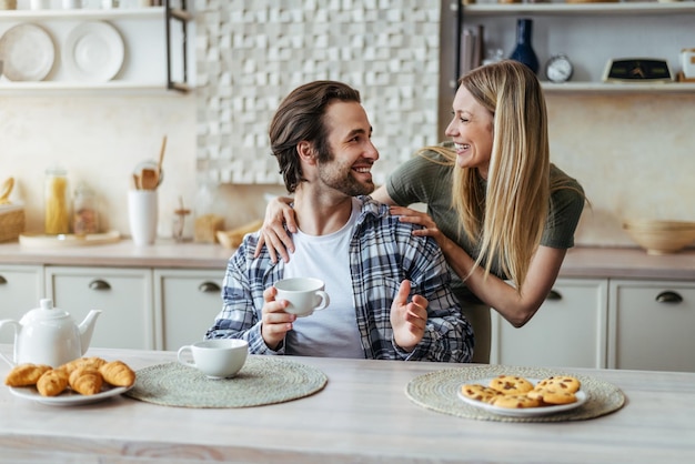 Cheerful young caucasian wife look at husband drinking coffee and talking in free time in modern