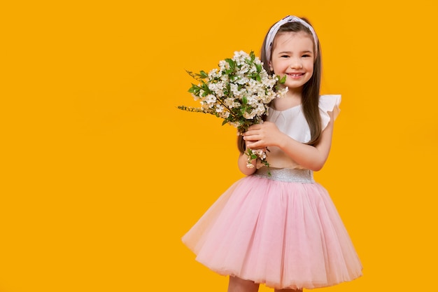 Cheerful young child with spring flowers in hands on bright yellow wall