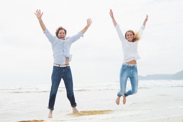 Cheerful young couple jumping at beach