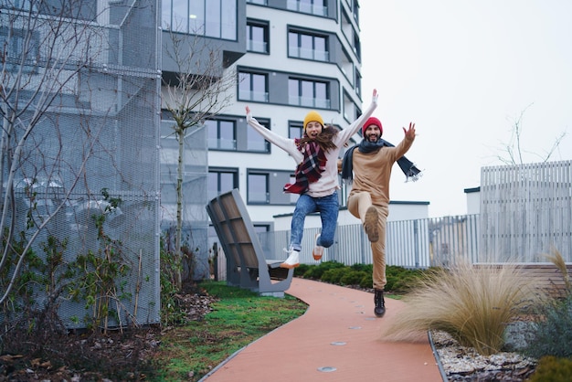 A cheerful young couple owners jumping outdoors in front of new flat