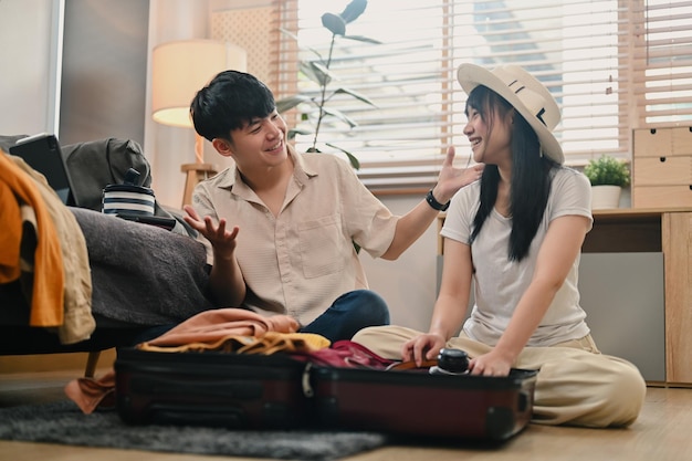 쾌활 한 젊은 부부 가 거실 에서 휴가 여행 을 준비 하고 있는 가방 에 옷 을 포장 하고 있다