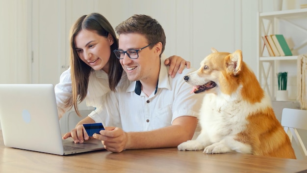 Cheerful Young Couple Shopping Online While Sitting Home With Credit Card and Laptop Computer. Mutual Family's Purchases. Purchase Confirmation by the Internet. Binding a Card for Online Shopping