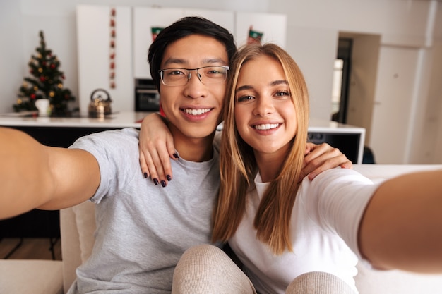 Cheerful young couple, sitting on a couch at home, taking a selfie