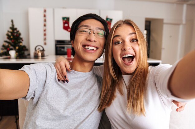 Cheerful young couple, sitting on a couch at home, taking a selfie