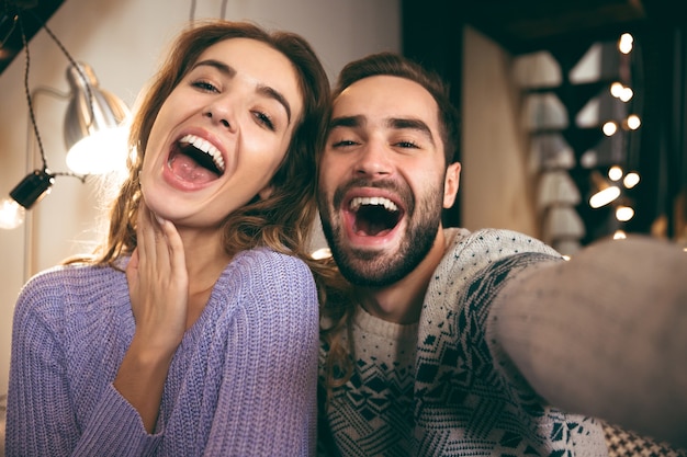 Allegro coppia giovane seduti insieme su un divano a casa, prendendo un selfie