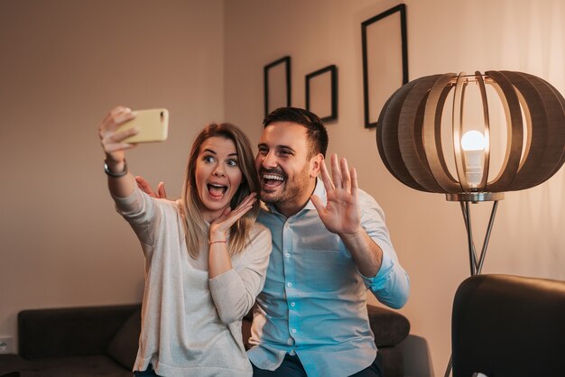 Cheerful young couple taking selfie indoors.