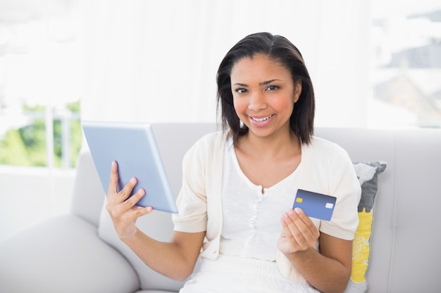 Cheerful young dark haired woman in white clothes shopping online with a tablet pc