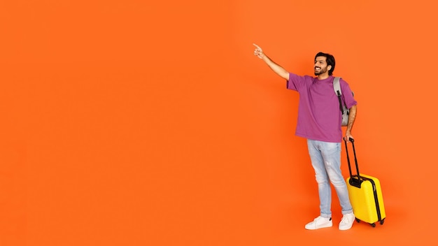 Cheerful young eastern man with backpack luggage showing empty space