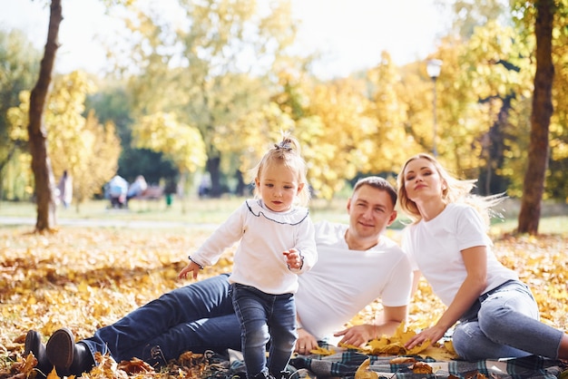 Cheerful young family lying down on the ground and have a rest in an autumn park together.