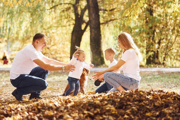 Cheerful young family with dog have a rest in an autumn park together.
