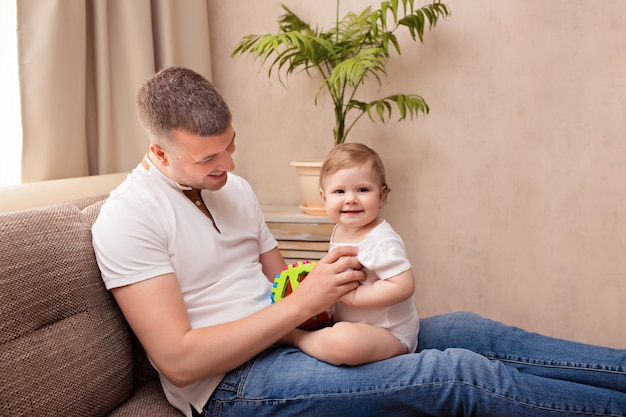 Cheerful young father is playing with his little daughter, spending time together and having fun on the couch