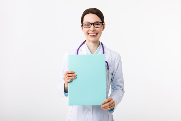 Cheerful young female doctor holding a folder in her hand and gesturing to copyspace