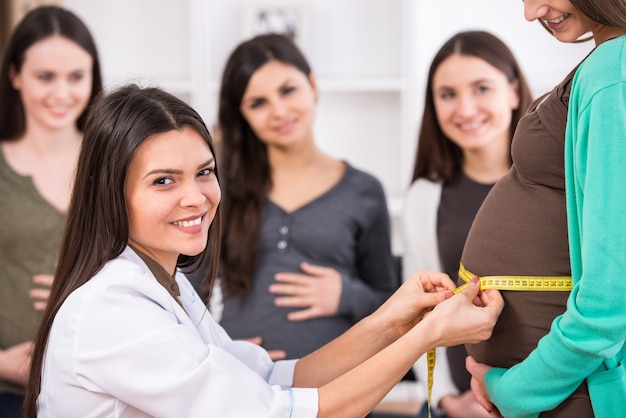 Cheerful young female doctor is measuring belly.