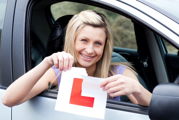 Веселая молодая женщина-водитель, рвущая свой знак L
