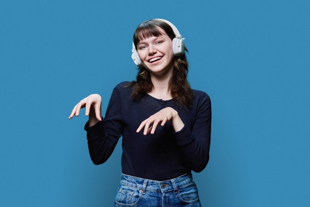 楽しい若い女性がヘッドホンで青い背景でトレンディなダンスを踊っています
