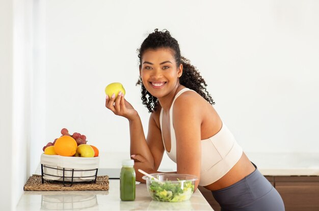 Foto giovane donna di fitness allegra che tiene una mela fresca in cucina