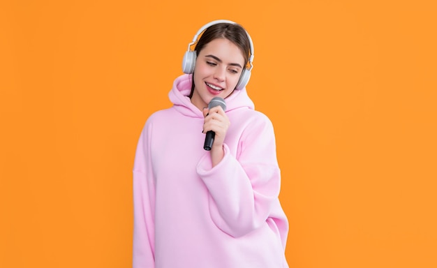 cheerful young girl in headphones with microphone on yellow background