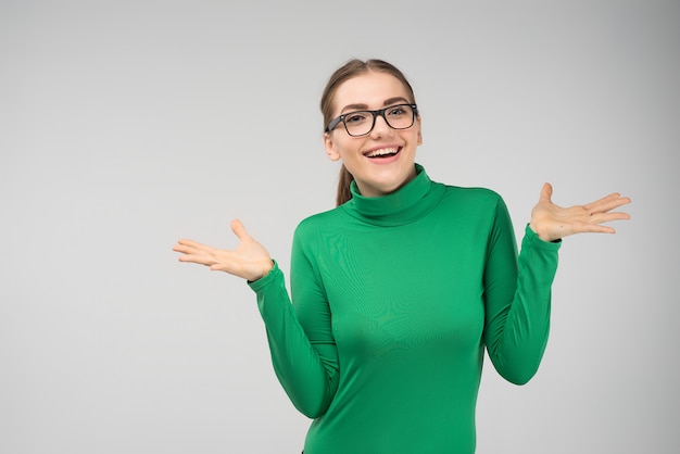 Cheerful young girl posing in studio shrugs in surprise