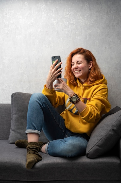 Cheerful young girl sits on the sofa and shoots stories. Chatting video call.