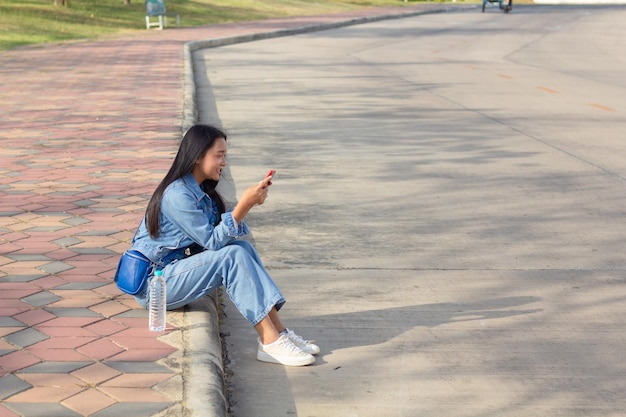 都市の公園に座っている陽気な若い女の子は、側のライフ スタイル コンセプトに置かれた水のボトルと携帯電話を保持します。