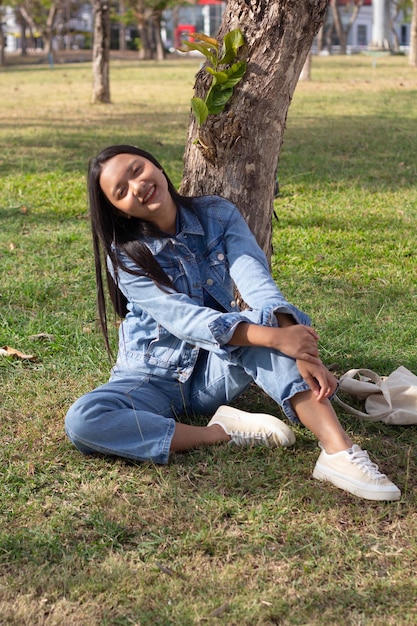 笑顔で公園に座っている陽気な若い女の子と身に着けているジャケットとジーンズのライフ スタイル コンセプト