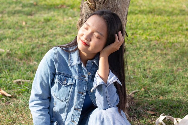 Cheerful young girl sitting in the park smiling and wears jacket and jeans lifestyle concept