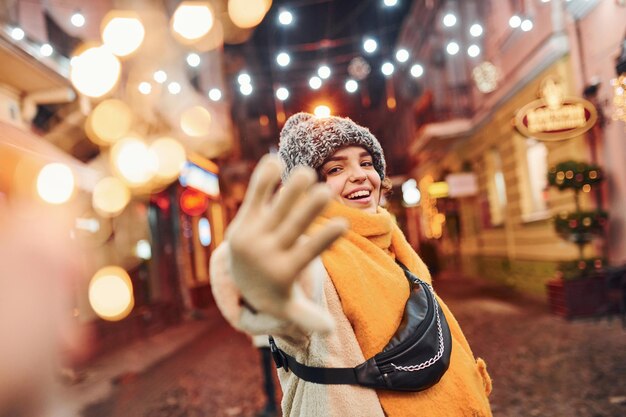 Cheerful young girl in warm clothes have a walk on the christmas decorated street in the city.