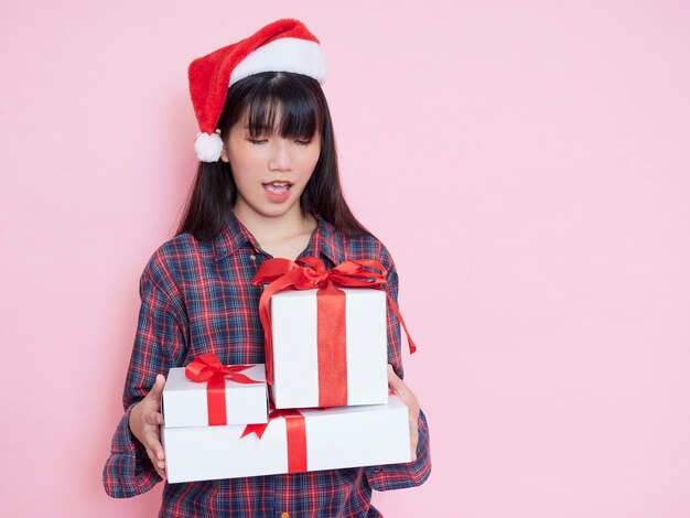 Cheerful young girl wearing santa hat with holding gift boxes on pink background