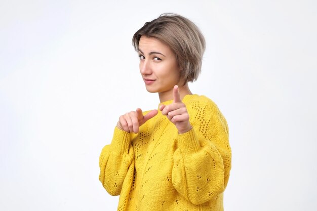 Cheerful young girl in yellow sweater pointing finger at camera