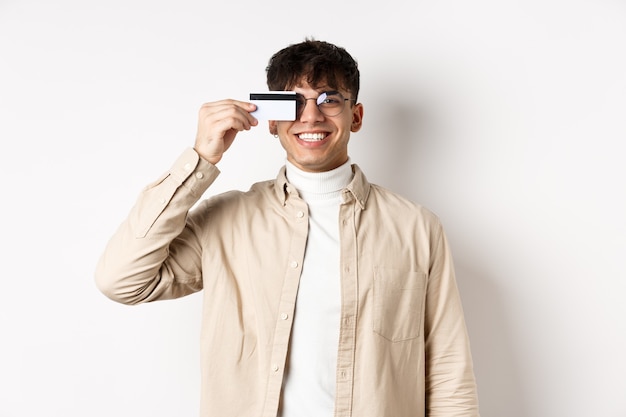 Cheerful young guy smiling real and showing plastic credit card standing happy on white background w...