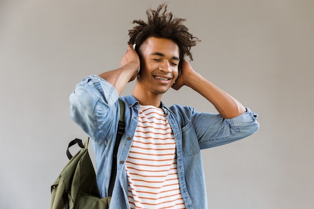 Cheerful young guy standing outdoors listening music with headphones