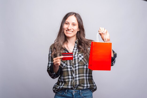 Cheerful young hipster woman holding credit card and shopping bag.
