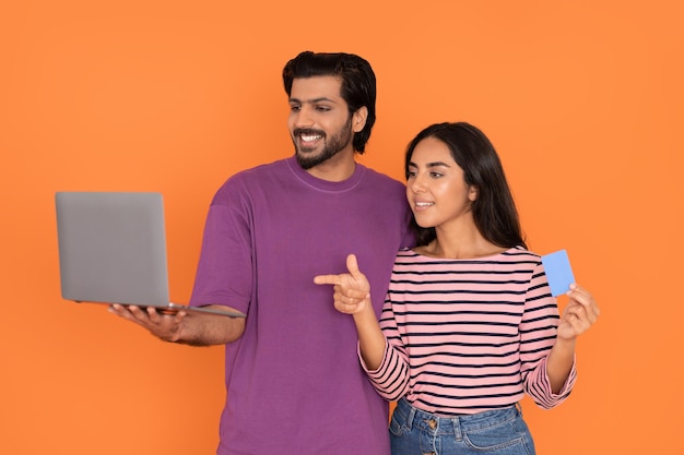 Cheerful young indian couple with laptop and bank card