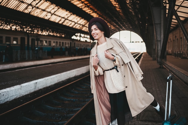 陽気な若い女性が駅で電車を待っています。