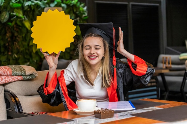 Cheerful young lady wearing graduation cape and holding idea board