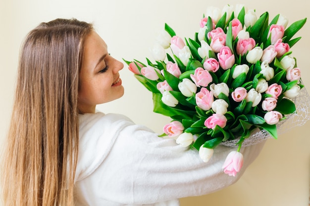 分離された女性の日にピンクのチューリップの花束を取得するために興奮している長い髪の陽気な若い女性