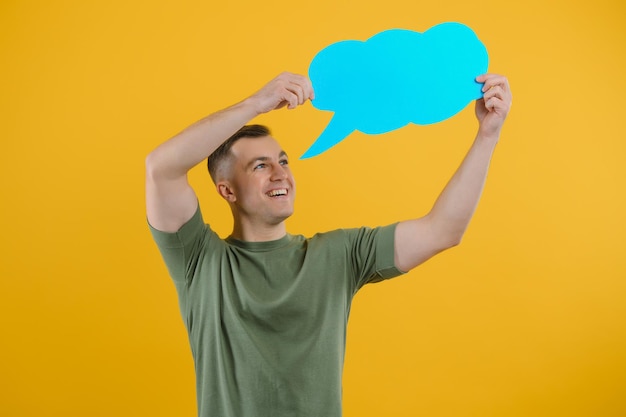 Cheerful young male pointing up and holding empty speech bubble with blank space for quote against vivid yellow background