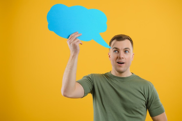 Cheerful young male pointing up and holding empty speech bubble with blank space for quote against vivid yellow background