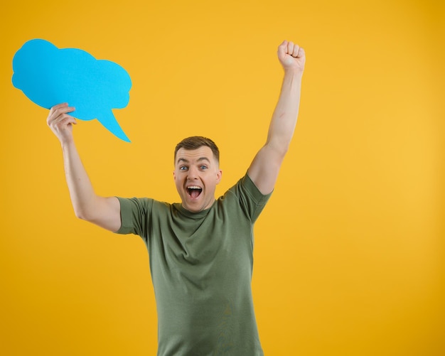 Cheerful young male pointing up and holding empty speech bubble with blank space for quote against vivid yellow background